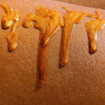 texture shot of the golden glitter shimmer oil dripping down a womans leg to show the pigmentation of the boil on black skin