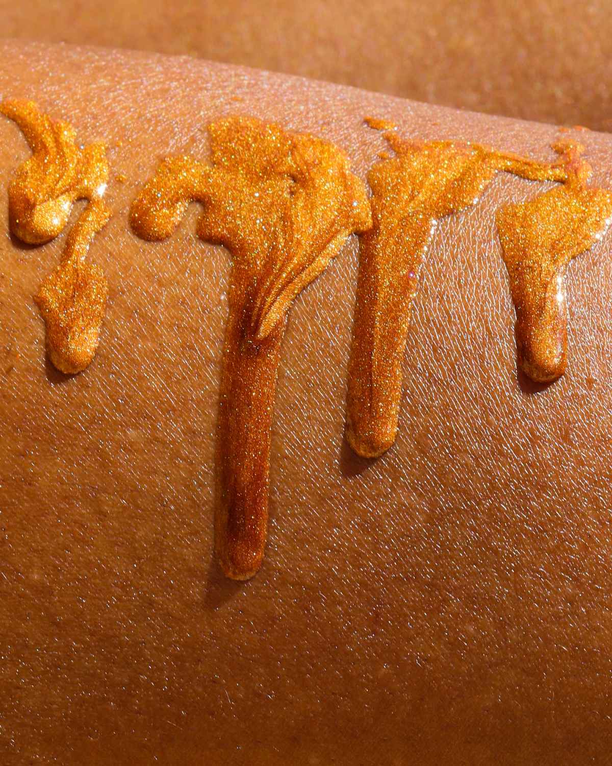 texture shot of the golden glitter shimmer oil dripping down a womans leg to show the pigmentation of the boil on black skin
