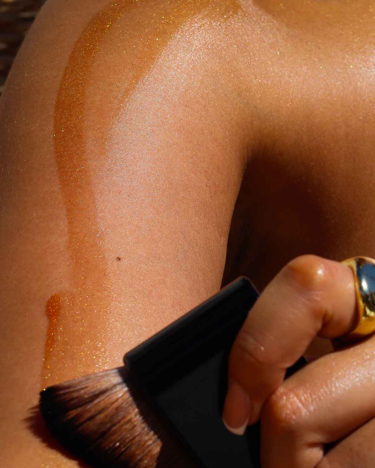 a photo of the body applicator brush applying our attention seeker bronzing shimmer oil on medium skin