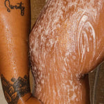 a shower shot of the strip tease sugar vanilla body scrub being applied in the shower on legs to tackle dry skin, bumpy areas, dark inner thighs, and dark marks
