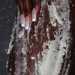 a photo of a womans leg showing vanilla body scrub application for hyperpigmentation, dull skin, body acne and strawberry legs, dry knees and elbows