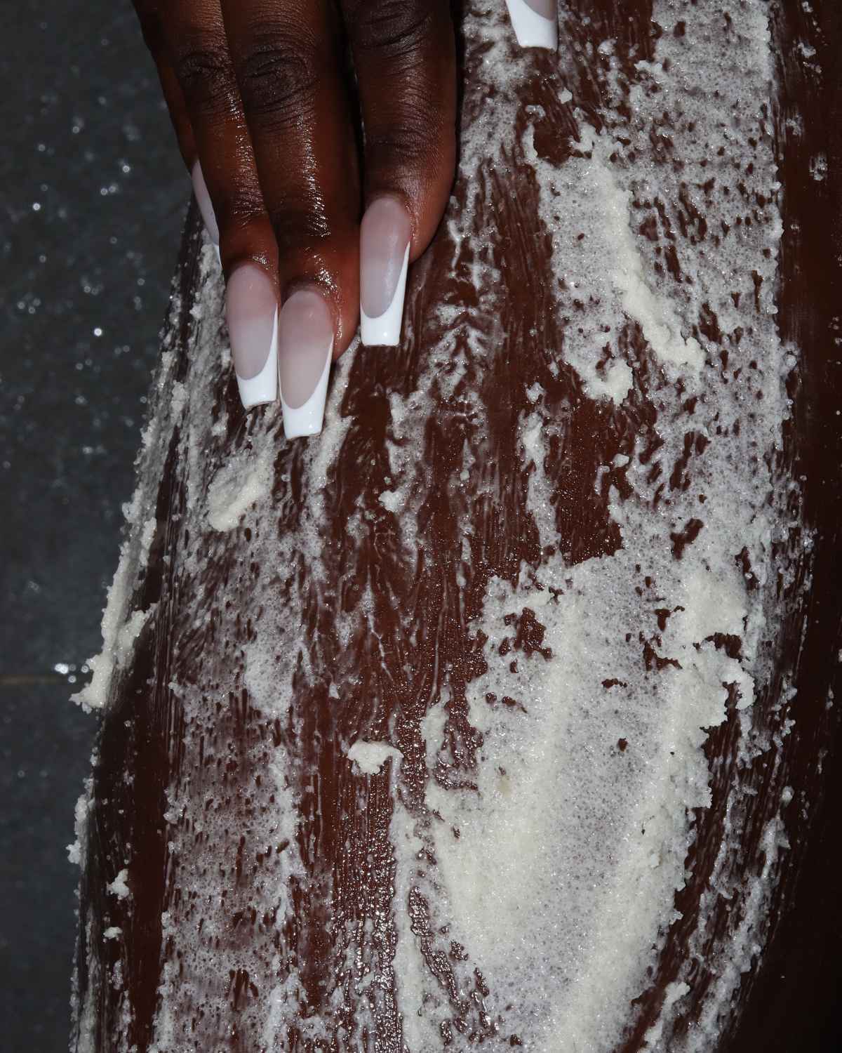 a photo of a womans leg showing vanilla body scrub application for hyperpigmentation, dull skin, body acne and strawberry legs, dry knees and elbows