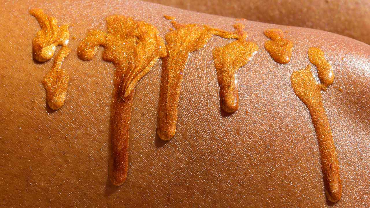 texture shot of the golden glitter shimmer oil dripping down a womans leg to show the pigmentation of the boil on black skin